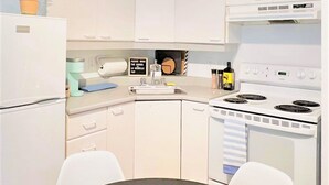 Cocina compacta con gabinetes blancos, estufa, lavamanos y una pequeña mesa de comedor.