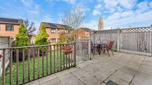 Eine Terrasse mit Tisch und Stühlen, ein Holzzaun und ein Garten mit Baum und Rasen.