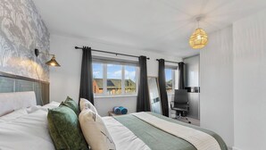 Ein Schlafzimmer mit Bett, Schreibtisch, Stuhl, Lampe und einem Fenster mit Vorhängen.