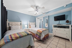 A bedroom with two beds, a ceiling fan, a TV, and a dresser. - Castaways 4A 🌊 Gulf Front Condo with Balcony + Pool (Gulf Shores)