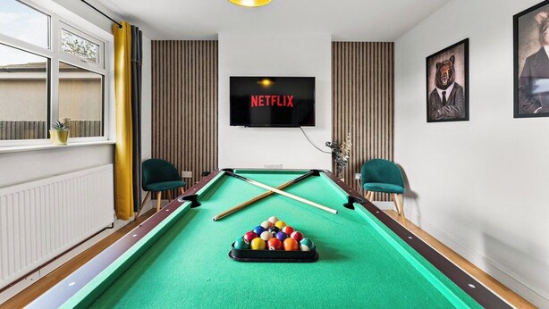 A pool table with a cue stick, a television mounted on the wall, and two chairs. - Stylish Langley Mill Stay | Sleeps 11 (Langley Mill)