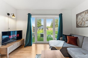 A living room with a television, sofa, and a view of a garden through glass doors.