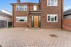 A two-story brick house with a central entrance door, a small porch, and a paved driveway.