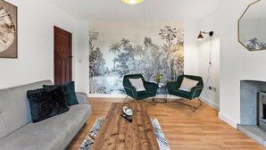 A living room with a sofa, two green armchairs, a wooden coffee table, and a mural of a tropical landscape. - Stylish Langley Mill Stay | Sleeps 11 (Langley Mill)