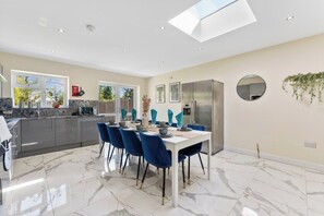 A modern kitchen with a dining area, featuring a large island, stainless steel appliances, and a skylight. - Stunning 6 bedroom in Wembley - Parking (London)