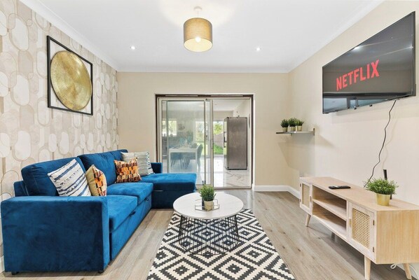 A modern living room with a blue sofa, a coffee table, and a TV mounted on the wall. - Stunning 6 bedroom in Wembley - Parking (London)