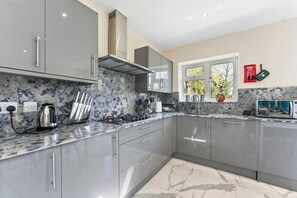 A modern kitchen with grey cabinets, a stainless steel range hood, and a window with a view of trees. - Stunning 6 bedroom in Wembley - Parking (London)