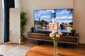 A flat-screen TV on a wooden stand, a potted plant, and a vase with flowers on a wooden table. - 1BR in a Landmark Tower  Rooftop Pool, 360° Views, Near Metro (Dubai)