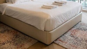 Una habitación de hotel moderna con una cama grande, una lámpara colgante, una ventana con cortinas y un cuadro en la pared.