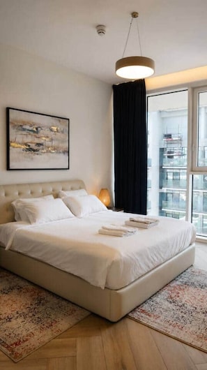 Habitació d'hotel moderna amb un llit gran, un penjoll, una finestra amb cortines i un quadre a la paret.
