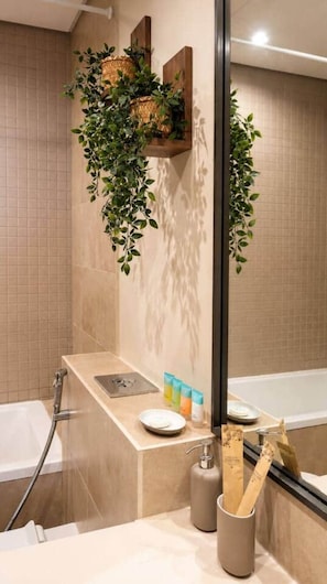 Un bany amb banyera, un lavabo amb articles de tocador i un mirall.