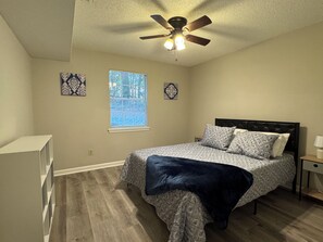 A bedroom with a bed, a ceiling fan, a window, and a nightstand.
