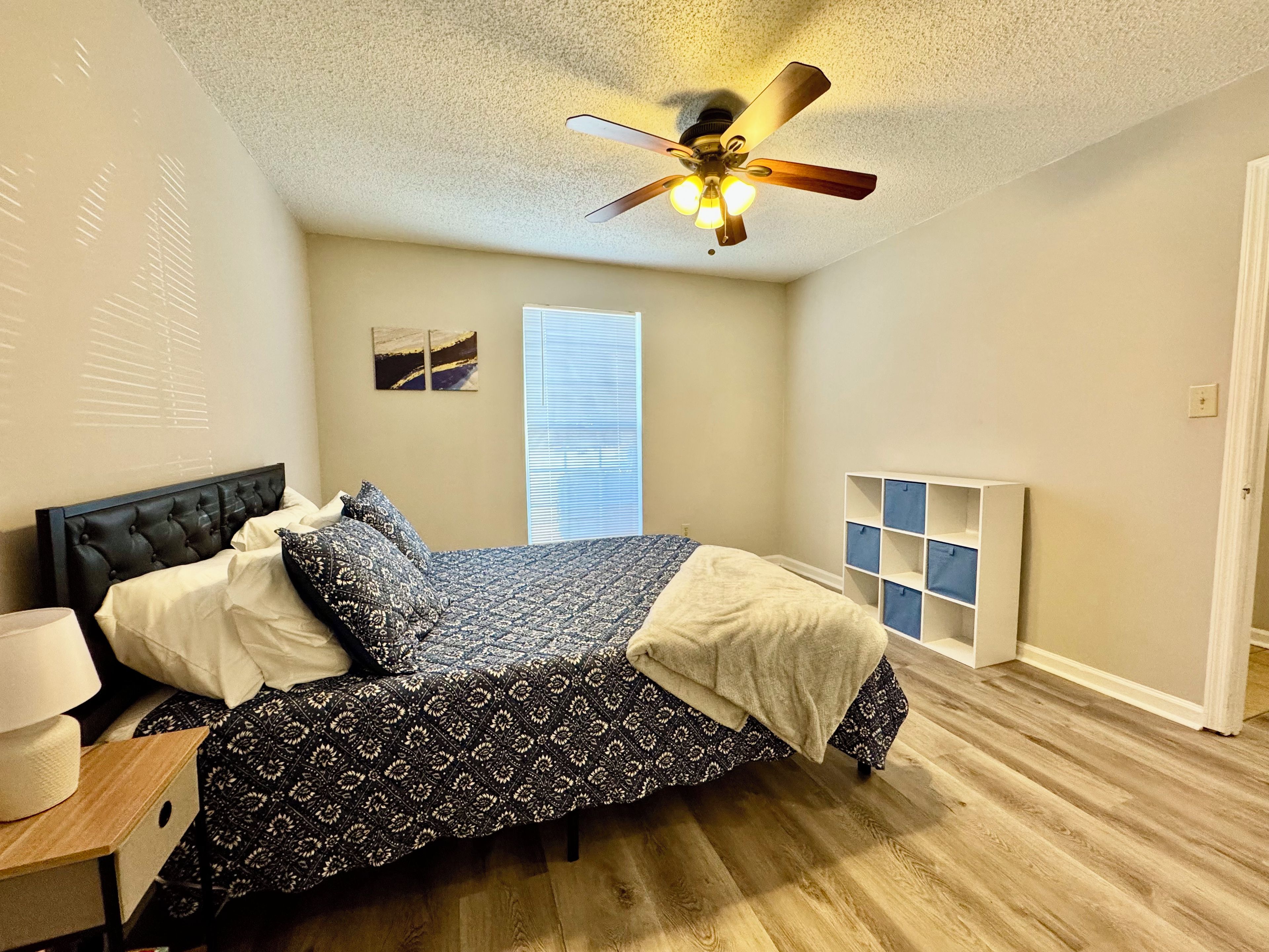 A bedroom with a bed, a nightstand, a ceiling fan, a window with blinds, and a white radiator.