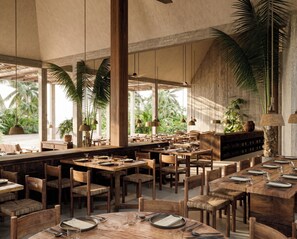 Un restaurante espacioso con techos altos, grandes ventanales y vistas a palmeras. Las mesas están dispuestas con platos, vasos y cubiertos.