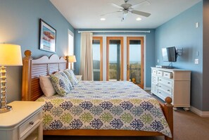 Une chambre à coucher comprenant un lit, une commode, un téléviseur et un ventilateur de plafond.