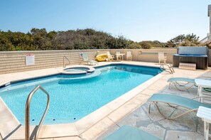 Une piscine extérieure rectangulaire, dotée d’un jacuzzi, entourée de chaises longues et d’un espace barbecue.