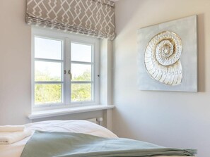 A bedroom with a bed, a window with a patterned valance, and a wall-mounted artwork. - Holiday Apartment Sylt 86 (Sylt)