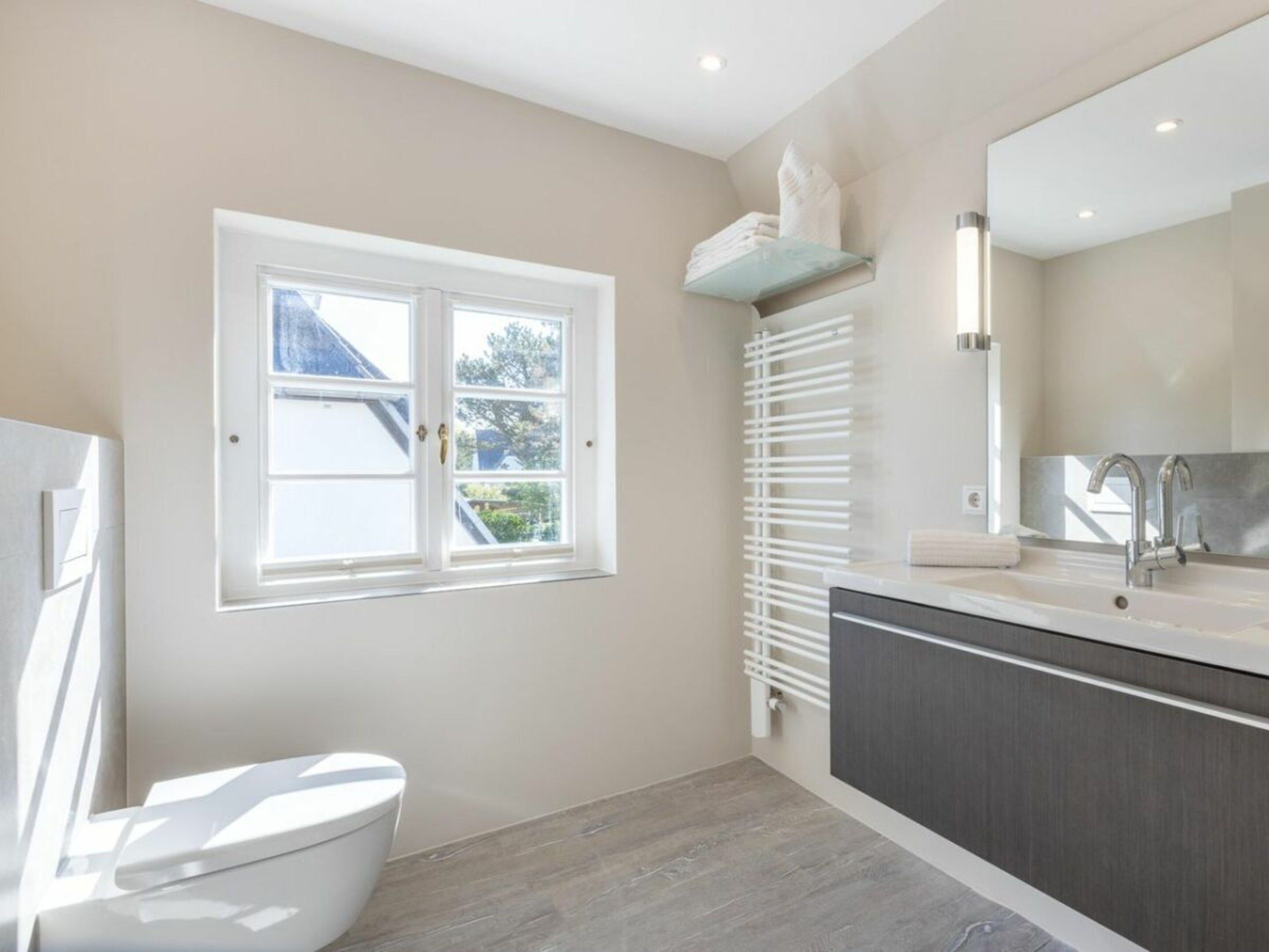 A bathroom with a toilet, a window, a radiator, and a sink with a mirror.