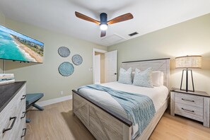 A bedroom with a bed, a nightstand, a TV, and decorative plates on the wall. - Hibis-Kiss Haven, Heated Pool, Walk To Dune Dog Restaurant (Jupiter)