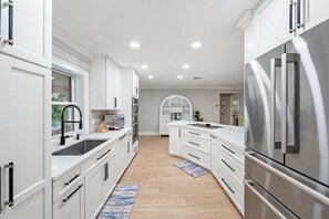 A modern kitchen with white cabinetry, stainless steel appliances, and a central island. - Hibis-Kiss Haven, Heated Pool, Walk To Dune Dog Restaurant (Jupiter)