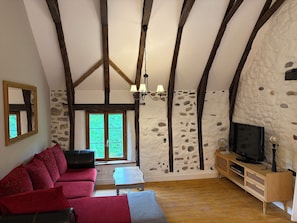 Una habitación con techo de madera, pared de piedra, un sofá, una mesita y un televisor.