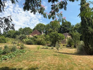 Una propiedad rural con una casa de piedra, un jardín con diversas plantas y un cielo despejado.