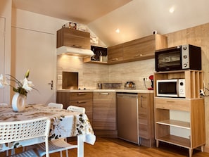 A compact kitchen with wooden cabinets, a stainless steel dishwasher, a microwave, and a table with a floral tablecloth. - Bright studio ski slopes view for (Les Deux Alpes)