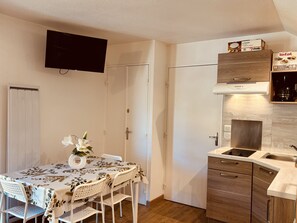 A compact kitchen with a built-in oven, a microwave, and a sink. There is a dining table with chairs and a vase of flowers. - Bright studio ski slopes view for (Les Deux Alpes)