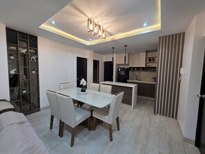 A modern kitchen with a central island, a dining area with a white table and chairs, and a built-in shelving unit with decorative items. - Comfortable Apartment in Cusco | Families and Groups (Cusco)