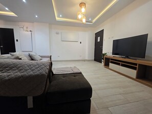 A modern bedroom with a bed, a bench, a TV, and a ceiling light fixture. - Comfortable Apartment in Cusco | Families and Groups (Cusco)