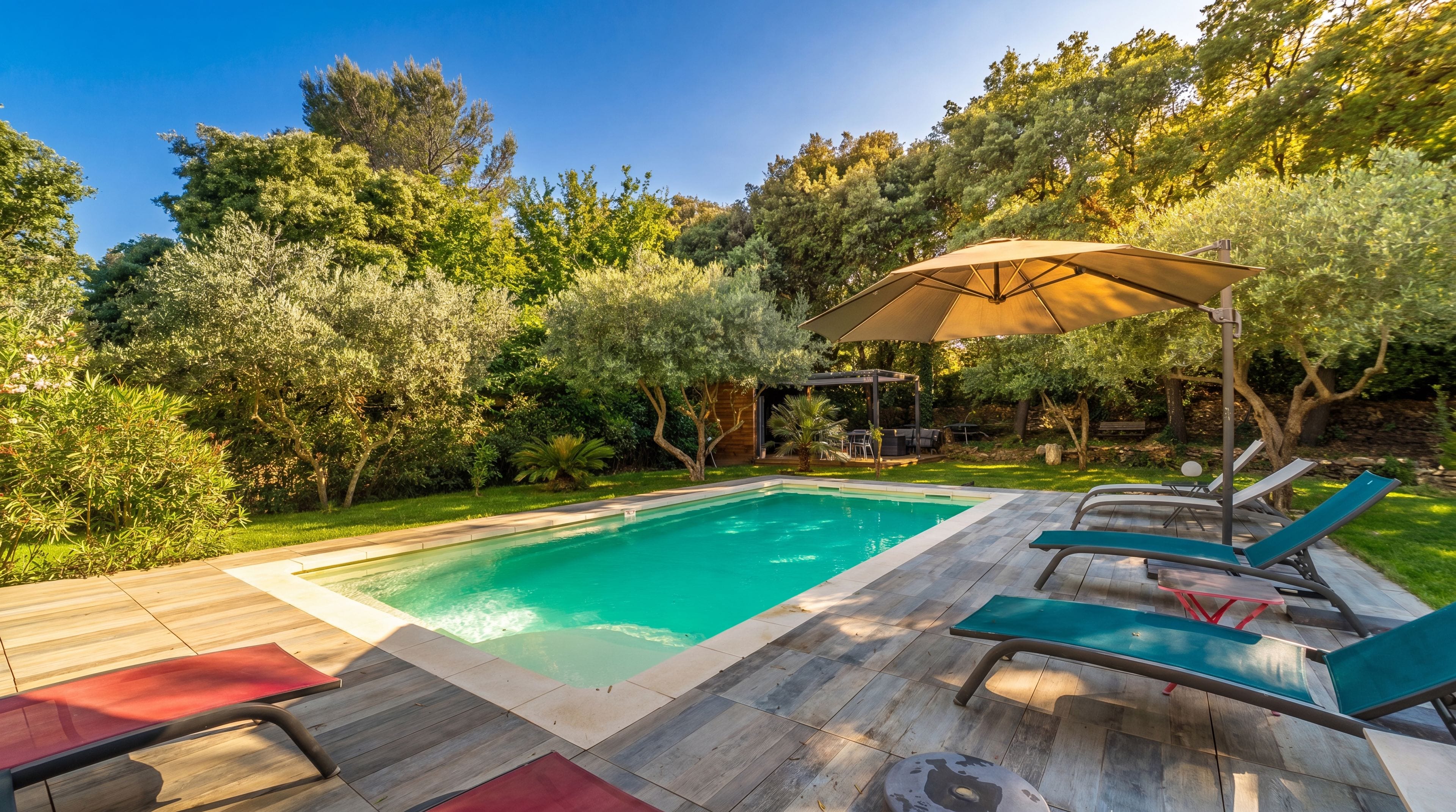 A swimming pool with a wooden deck, lounge chairs, and a pergola with an umbrella.