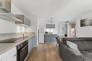 Eine moderne Küche mit Backofen, Mikrowelle und Spüle. Im Wohnbereich befindet sich ein graues Sofa und ein Esstisch mit Stühlen.