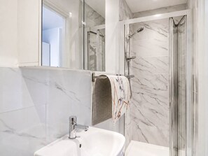 Ein modernes Badezimmer mit Marmorwaschbecken, einer Duschkabine aus Glas und einem Handtuchhalter mit einem gemusterten Handtuch.