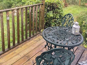 A wooden deck with a metal table and chairs, surrounded by greenery. - The Sheiling (Callander)