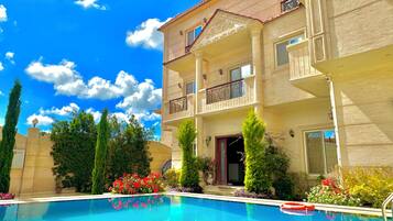 A hotel with a swimming pool, balconies, and a clear blue sky.