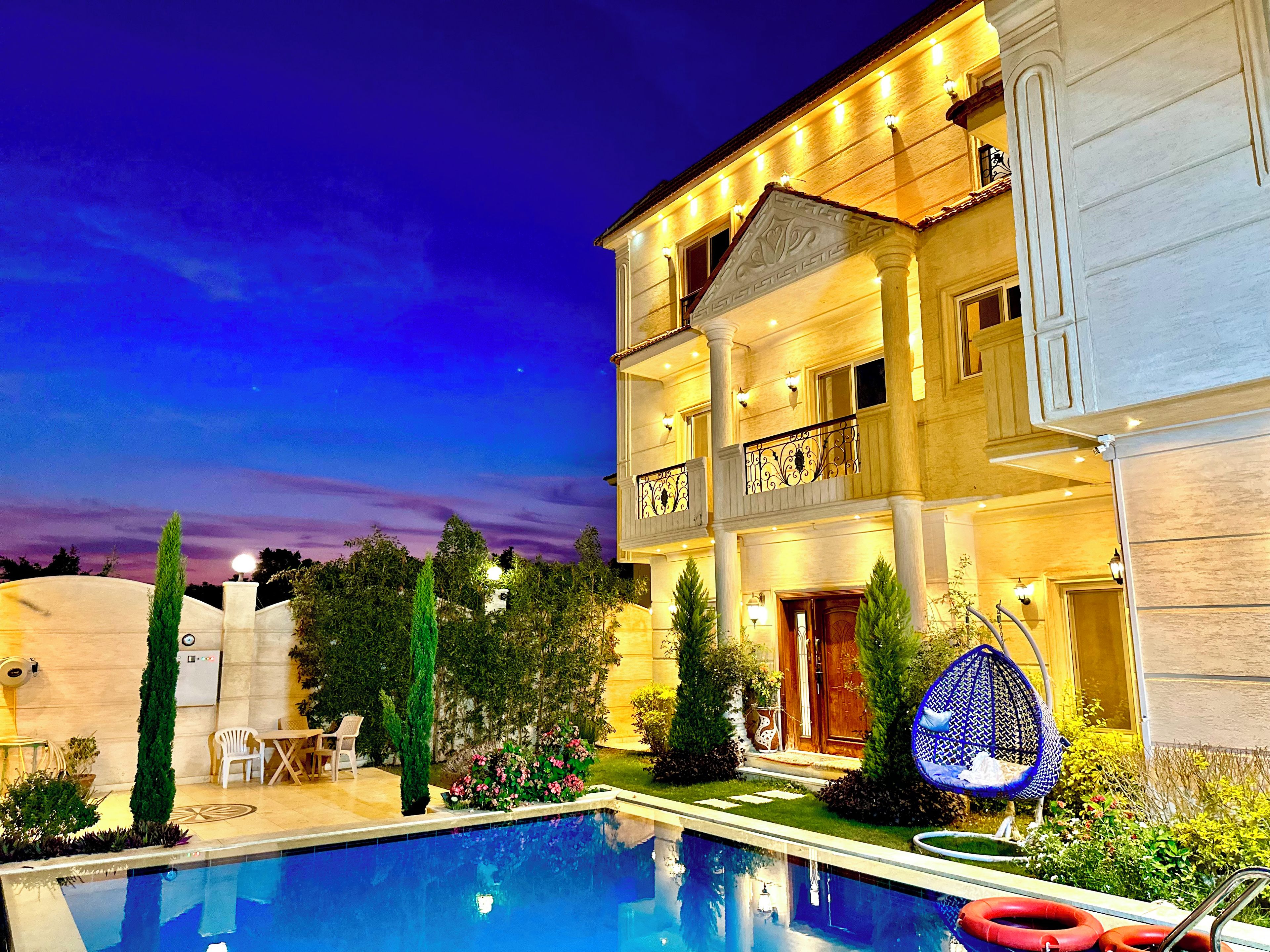 A multi-story hotel with a swimming pool, outdoor seating, and a well-lit facade.