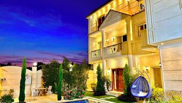 A multi-story hotel with a swimming pool, outdoor seating, and a well-lit facade.
