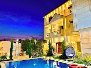 A multi-story hotel with a swimming pool, outdoor seating, and a well-lit facade.