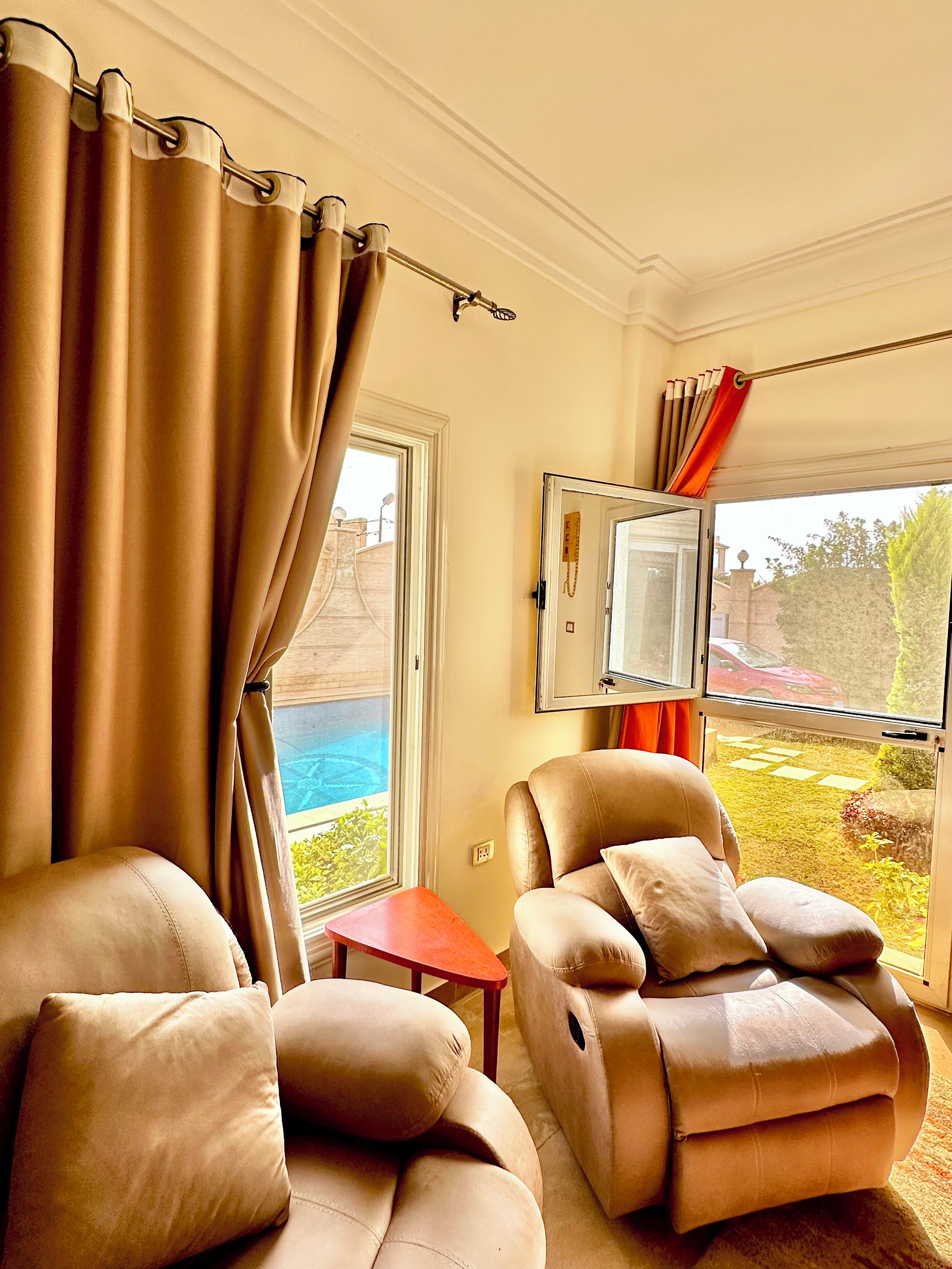 Ein Zimmer mit Massagesessel, einem kleinen Tisch und Blick auf Pool und Garten.