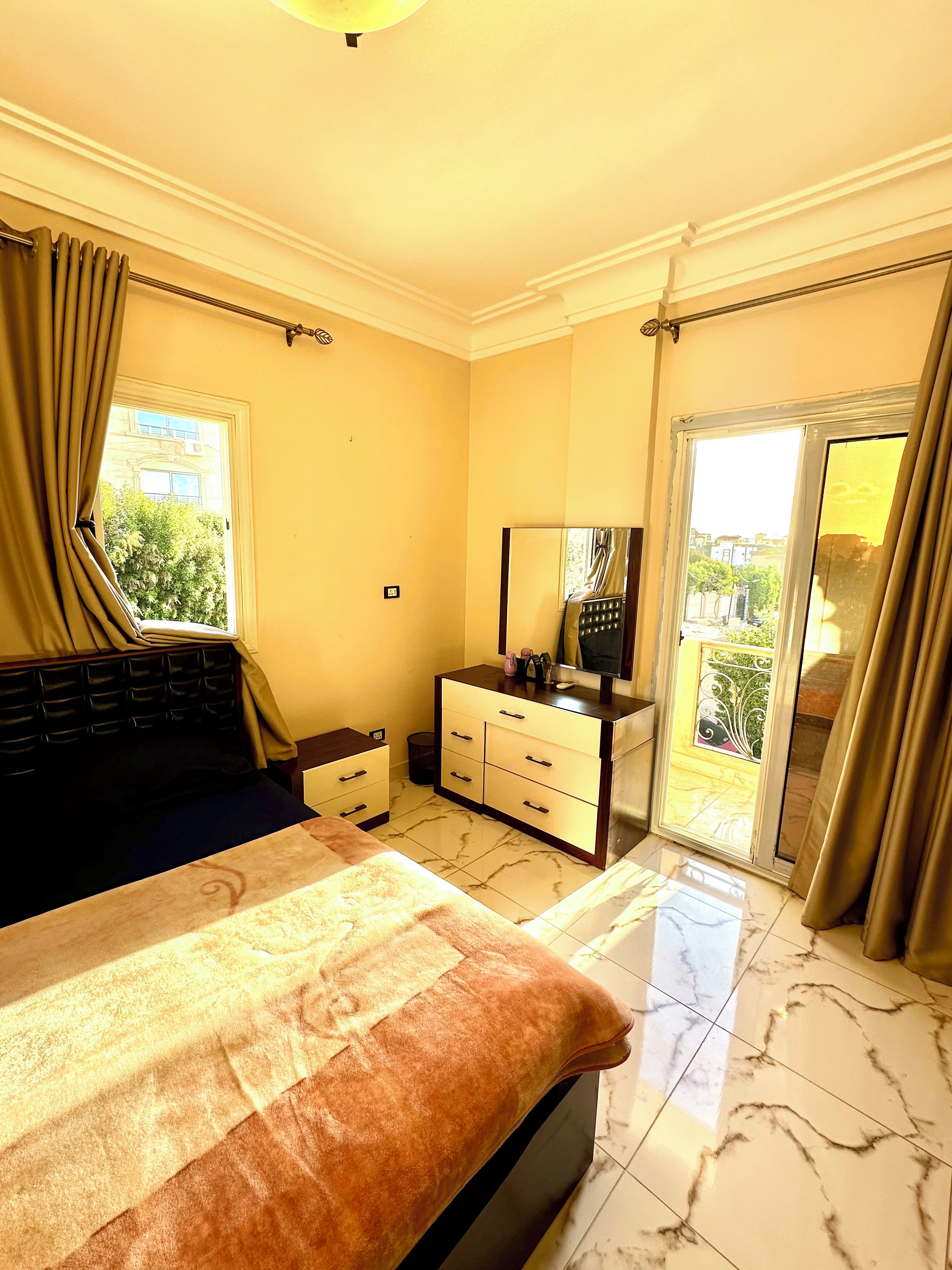 A hotel room with a bed, a dresser, a mirror, and a sliding glass door leading to a balcony.