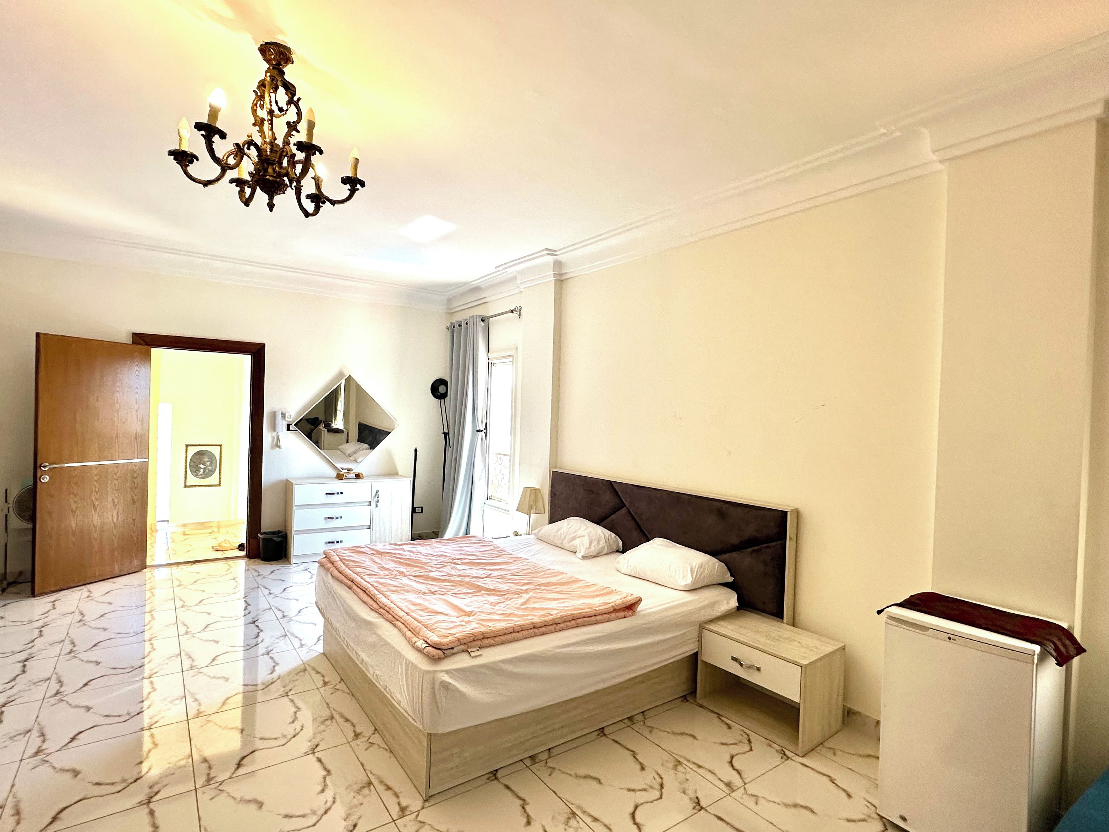 A bedroom with a bed, bedside tables, a mirror, a chandelier, and a wardrobe.