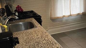 A kitchen with granite countertops, a stove, a sink, and a window with curtains.