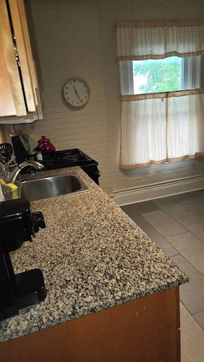 A kitchen with granite countertops, a stove, a sink, and a window with curtains.
