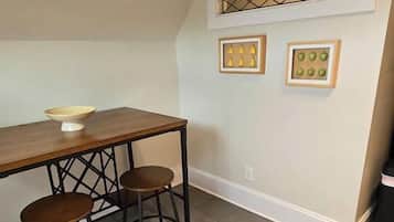Una cocina con una mesa de madera y dos taburetes, una ventana con diseño de celosía y cuadros en la pared.