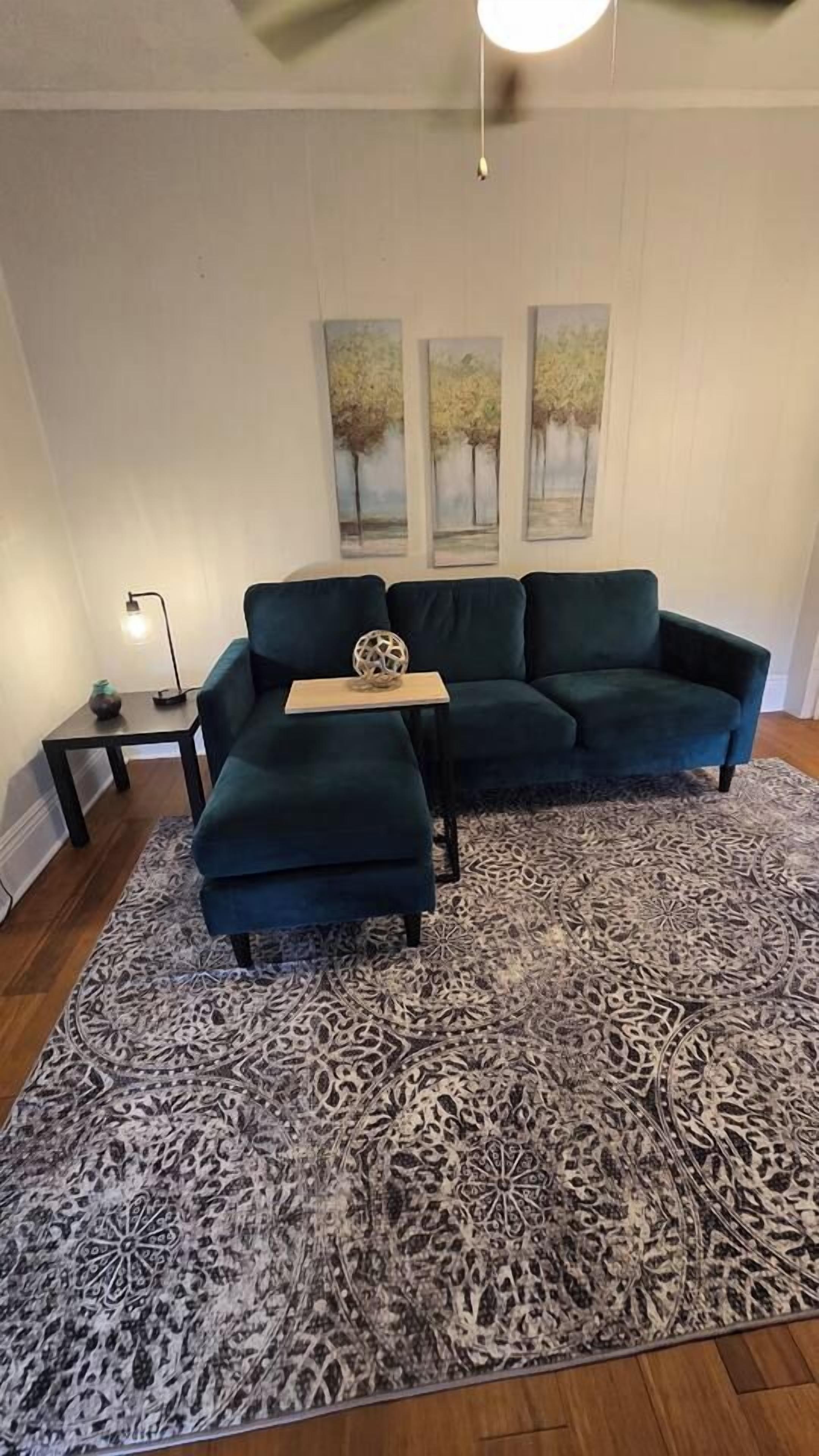 A living room with a sectional sofa, a patterned rug, and wall art.