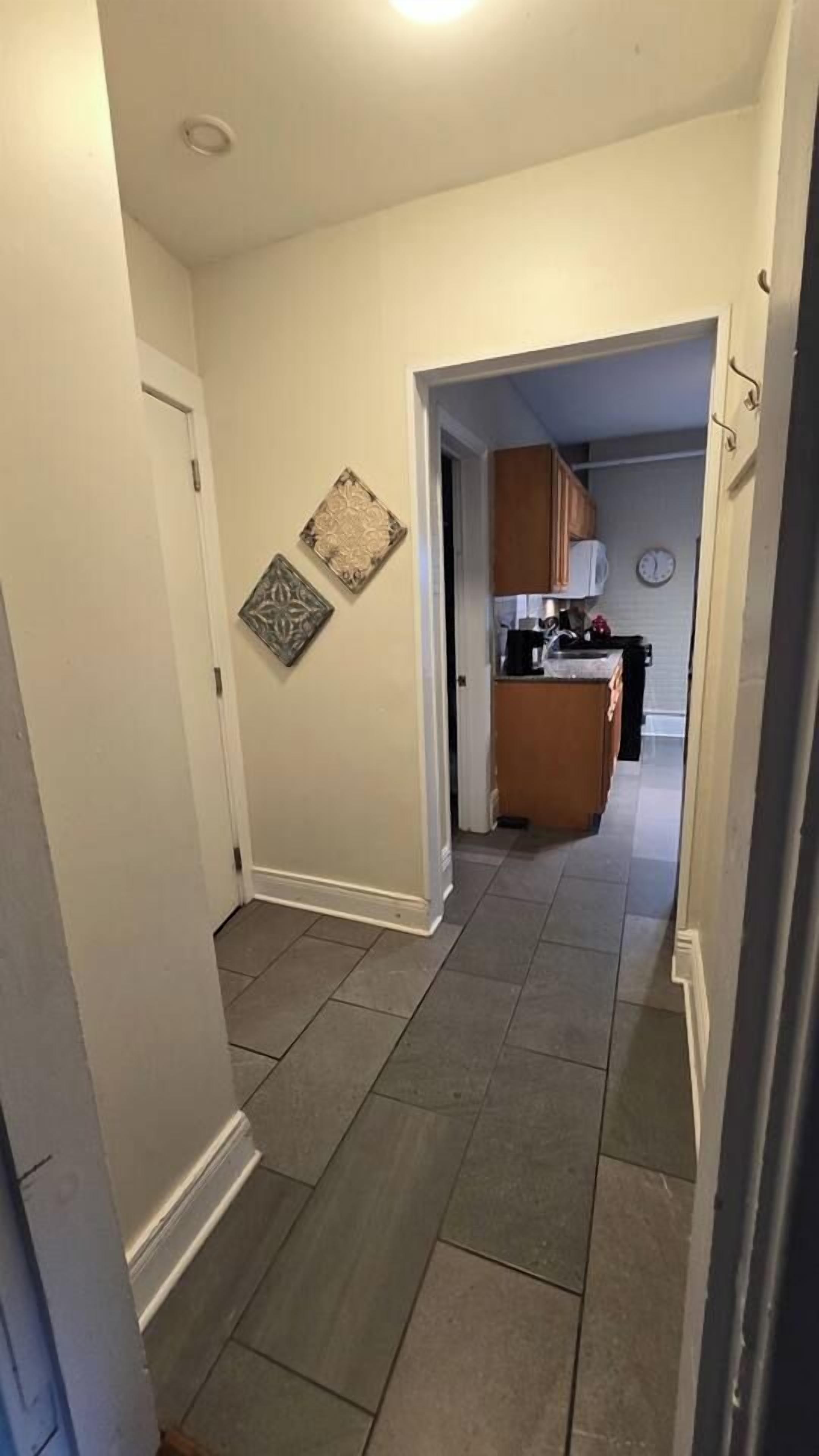 Un pasillo con una zona de cocina al fondo, que presenta suelo de baldosas y un reloj en la pared.