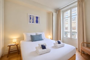 A hotel room with a bed, bedside lamps, a window with curtains, and a view of buildings outside. - Elegant Apartment Arc de Triomphe Trocadero (Paris)