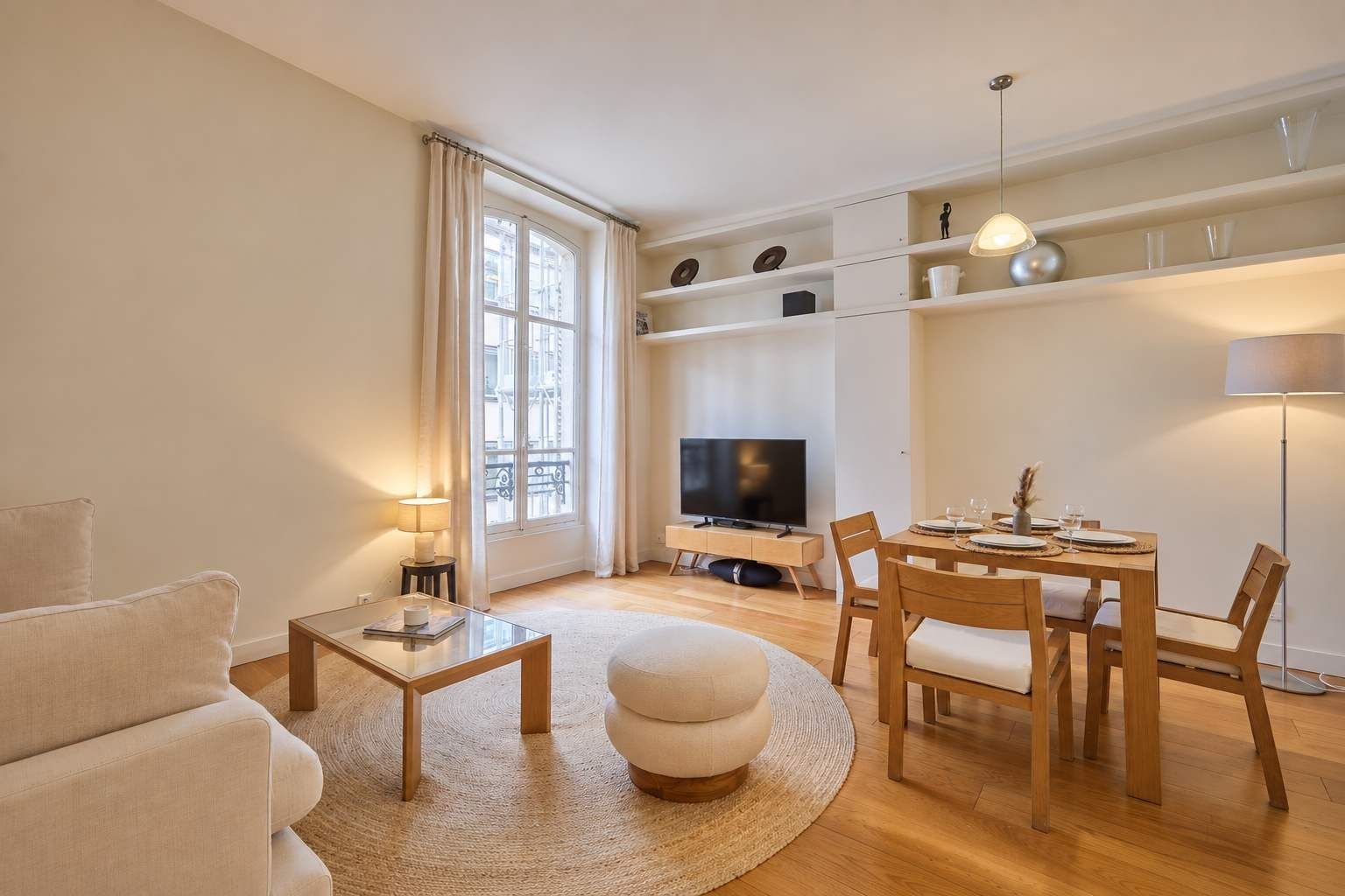 A modern living room with a sofa, a coffee table, a TV, a dining table with chairs, and a lamp.
