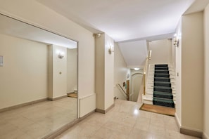 A hallway with a mirrored wall, a staircase, and a door leading to another room. - Elegant Apartment Arc de Triomphe Trocadero (Paris)