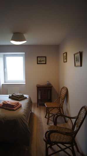 Ein Schlafzimmer mit einem Bett, zwei Stühlen, einem kleinen Tisch und einem Fenster.